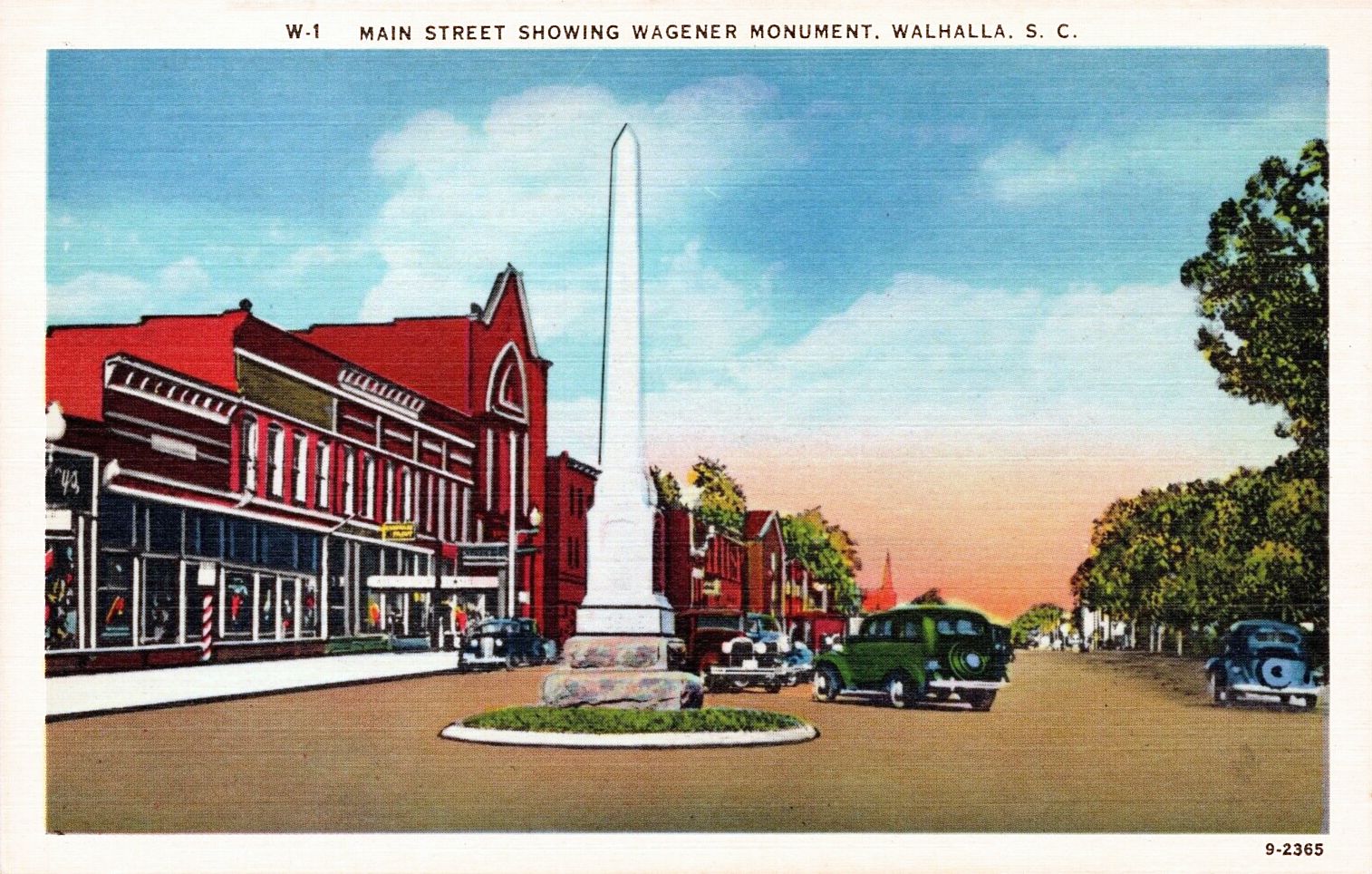 Postcard of Main Street in Walhalla with the white Wagener monument, red brick storefronts and 1930s cars.